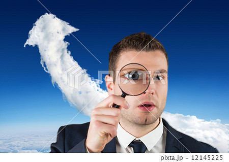 Composite image of businessman looking through magnifying glass 12145225