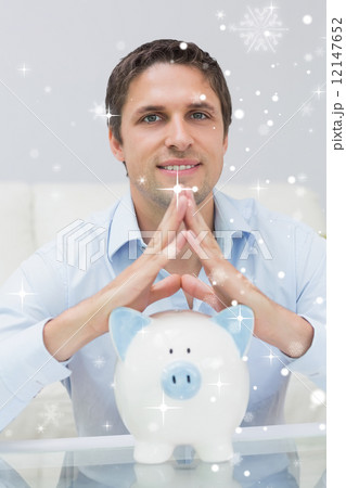 Composite image of handsome casual man with piggy bank in living Composite image of handsome casual man with piggy bank in living 12147652