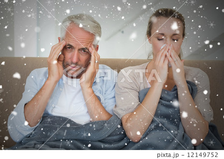 Composite image of sick couple sitting on the couch under a blan 12149752
