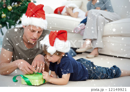 Father and son unwrapping a present lying on the floor 12149921