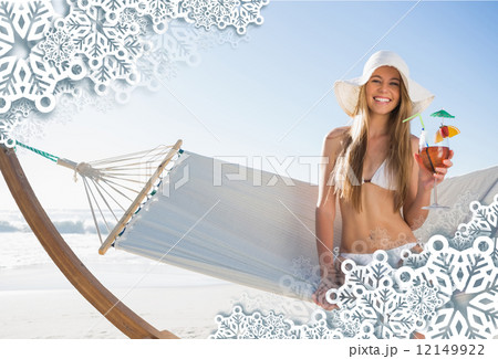 Smiling blonde wearing sunhat sitting on hammock with cocktail 12149922