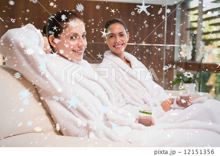 Smiling women in bathrobes sitting on couch 12151356