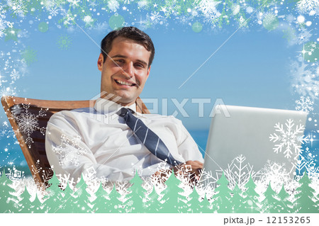 Cheerful young businessman lying on a deck chair with his comput 12153265