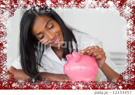 Smiling businesswoman putting coins into piggy bank at her desk 12153457