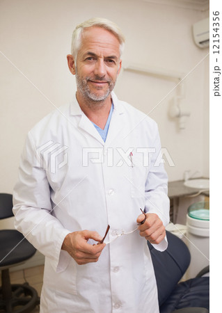 Dentist smiling at camera beside chair 12154356