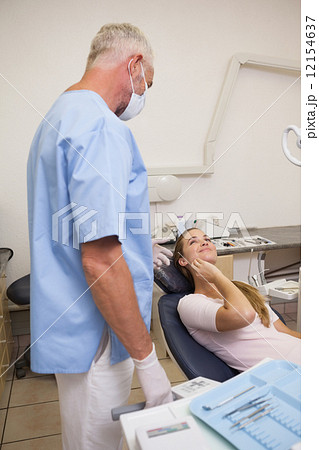 Patient lying in chair touching painful mouth looking at dentist 12154637
