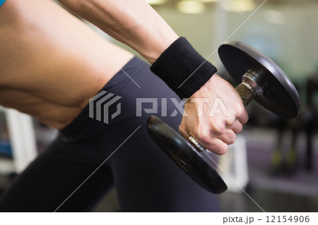 Mid section of fit woman exercising with dumbbell in gym Mid section of fit woman exercising with dumbbell in gym 12154906