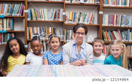 Cute pupils and teacher looking at camera in library 12154964
