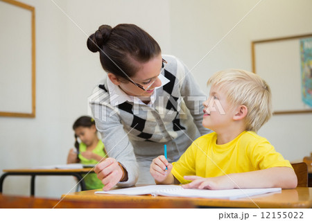 Pretty teacher helping pupil in classroom 12155022