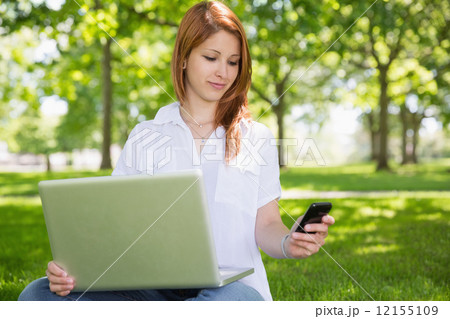 Pretty redhead using her laptop while texting in the park 12155109
