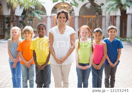 Pretty teacher standing with pupils in courtyard 12155245