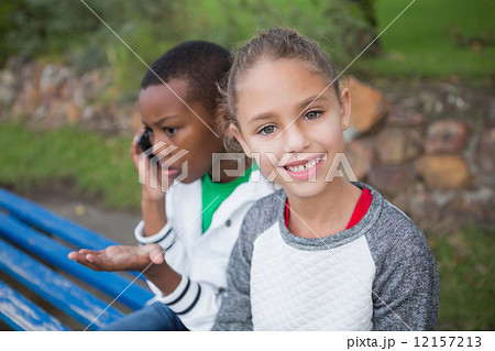 Cute little girl smiling at camera while friend talks on phone 12157213