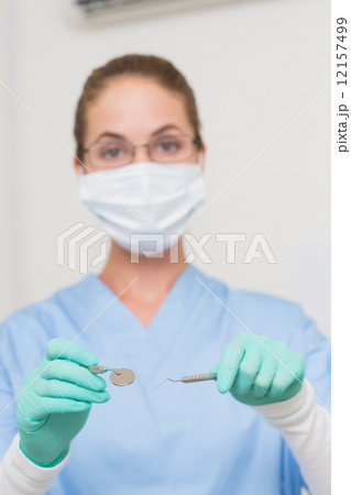 Dentist in blue scrubs holding tools looking at camera Dentist in blue scrubs holding tools looking at camera 12157499