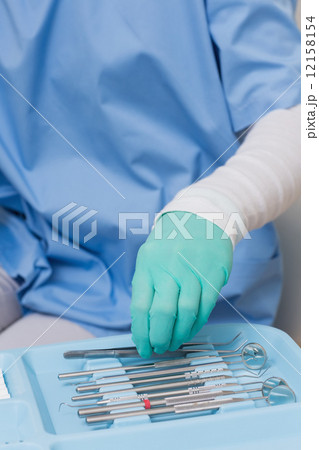 Dentist in blue scrubs picking up tools 12158154