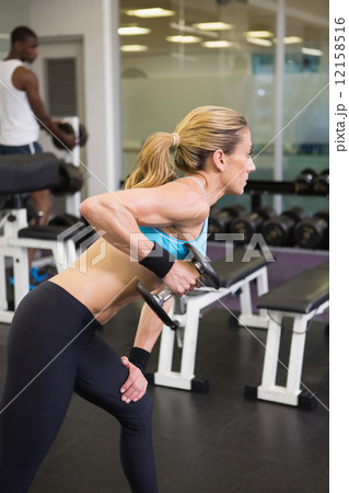 Side view of fit woman exercising with dumbbell in gym 12158516