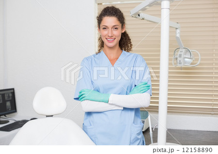 Dentist in blue scrubs smiling at camera beside chair 12158890