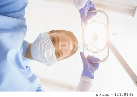 Dentist in surgical mask shining light over patient 12159148