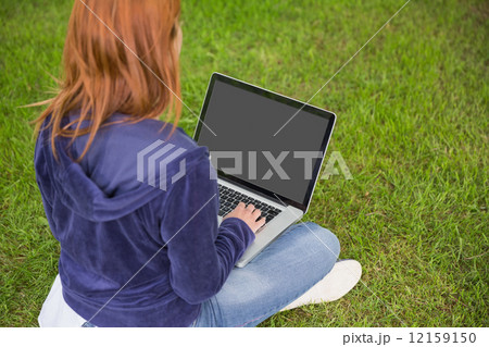 Pretty redhead relaxing in the park using laptop 12159150