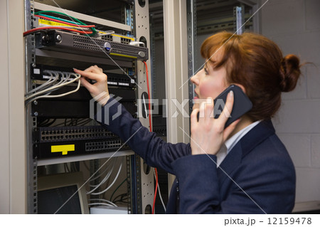 Pretty technician talking on phone while fixing server Pretty technician talking on phone while fixing server 12159478