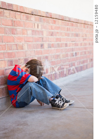 Sad pupil sitting alone in corridor 12159480