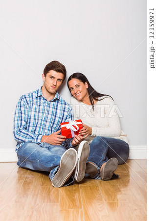 Young couple sitting on floor with gift Young couple sitting on floor with gift 12159971