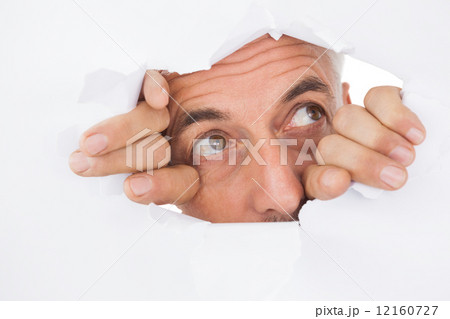 Man peeking through torn white surface Man peeking through torn white surface 12160727