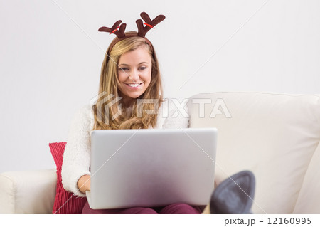 Festive blonde relaxing on sofa with laptop 12160995