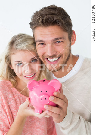 Attractive young couple holding piggybank Attractive young couple holding piggybank 12163496