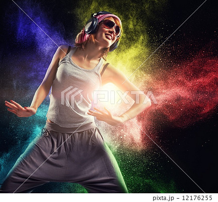 Stylish teenage girl with headphones dancing against colourful powder explosion 12176255