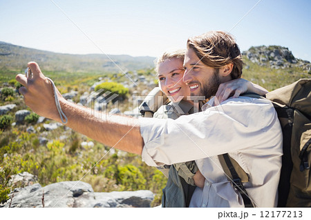 Hiking couple standing on mountain terrain taking a selfie Hiking couple standing on mountain terrain taking a selfie 12177213