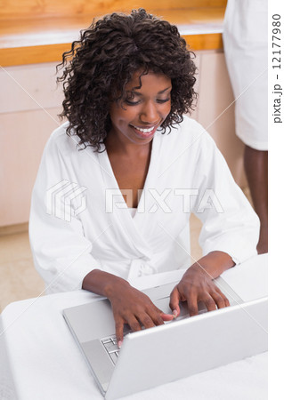 Pretty woman in bathrobe using laptop at table with partner in b Pretty woman in bathrobe using laptop at table with partner in b 12177980