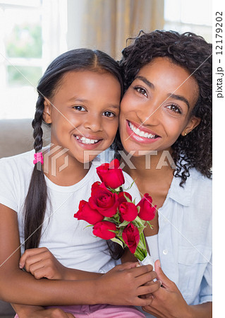 Pretty mother sitting on the couch with her daughter holding ros Pretty mother sitting on the couch with her daughter holding ros 12179202