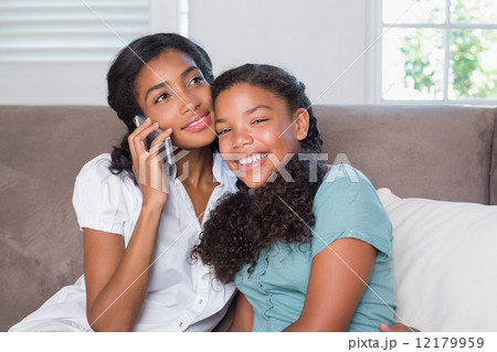 Happy mother and daughter using smartphone together on sofa 12179959