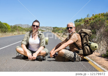 Hitch hiking couple sitting on the side of the road looking at c 12179972