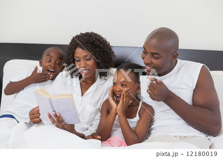 Family relaxing together in bed reading book 12180019