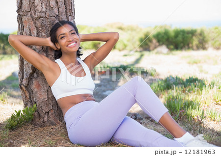 Fit woman sitting against tree smiling at camera 12181963