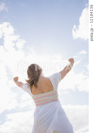 Woman with arms outstretched against blue sky and clouds 12184136