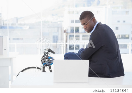 Serious businessman sitting on desk looking at laptop Serious businessman sitting on desk looking at laptop 12184344
