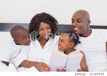 Happy family reading book together in bed 12184433