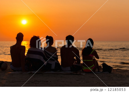 Silhouettes a young people sitting on a beach looking at sunset Silhouettes a young people sitting on a beach looking at sunset 12185053