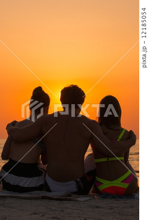 Silhouettes a young people sitting on a beach looking at  sunset 12185054