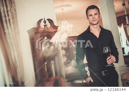 Handsome young well-dressed man in luxury house interior with glass of red wine 12186144