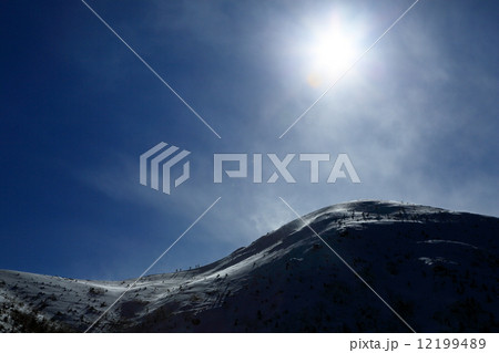 雪煙上がる厳冬の北八ヶ岳・東天狗岳と稜線を行く登山者 12199489
