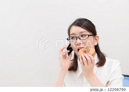 ドーナツを食べながら電話する女性 12206790