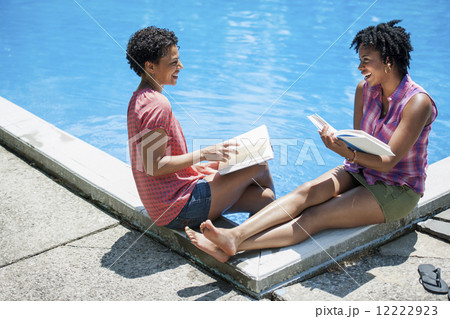 Two women sitting by the side of a swimming pool, reading books. Two women sitting by the side of a swimming pool, reading books. 12222923