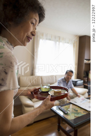 A woman serving a tray of food to a man sitting on a sofa. A woman serving a tray of food to a man sitting on a sofa. 12222997