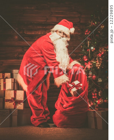 Santa Claus in wooden home interior with sack full of Christmas presents Santa Claus in wooden home interior with sack full of Christmas presents 12229895