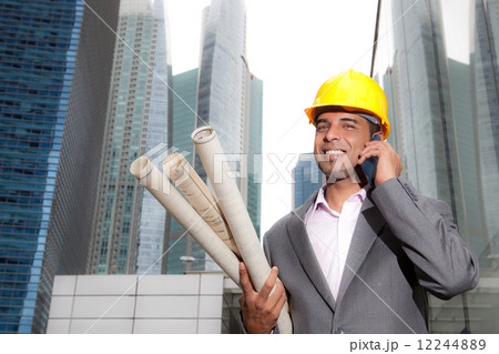 Asian business executive with hard hat and architectural plans on phone Asian business executive with hard hat and architectural plans on phone 12244889
