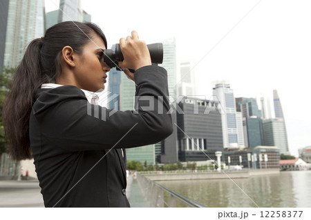 Businesswoman looking through binoculars outdoors 12258377