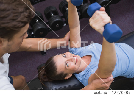 Personal trainer helping client lift dumbbells 12270207